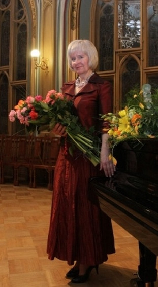 Ilze Arne pie klavierēm koncertzālē ar ziediem